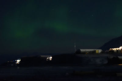 Illuminated buildings by street against sky at night