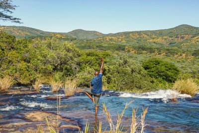 A man doing yoga pose at kimani river against sky at mpanga kipengele game reserve, tanzania