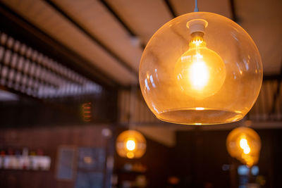 Close-up of illuminated light bulb hanging from ceiling