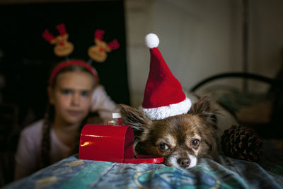 Girl and dog in santa red hat dreamily waiting for gifts near decorative mail box on christmas eve