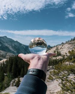 Cropped hand holding crystal ball against sky