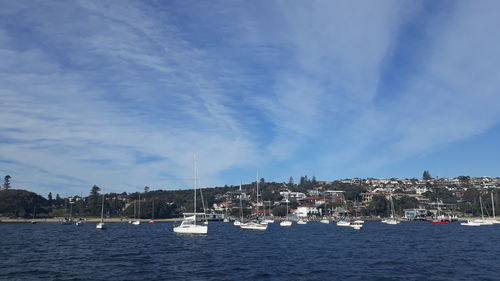 Sailboats moored on sea by buildings against sky