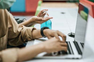 Midsection of businessman using laptop while colleague using hand sanitizer