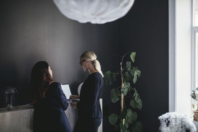 Female coworkers discussing over laptop on cabinet in home office