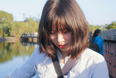 Close-up of smiling woman looking down against river on sunny day