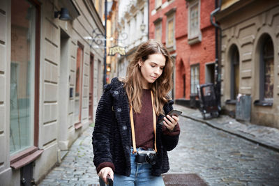 Young woman using mobile phone while standing in alley