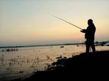 Silhouette man fishing on beach against clear sky