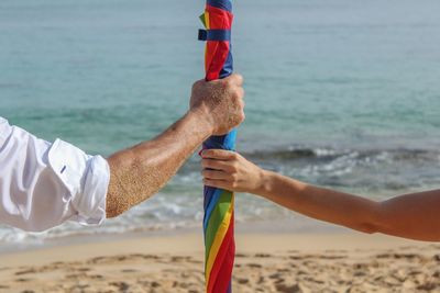 Cropped hands of couple holding colorful umbrella at beach