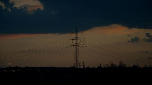 Silhouette electricity pylons on field against sky at sunset