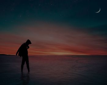 Silhouette man standing in sea against sky during sunset