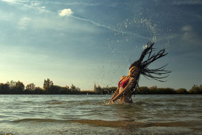 Side view of woman splashing water against sky