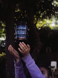 Close-up of hands below lantern hanging from tree