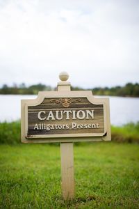 Close-up of information sign on grass by lake against sky