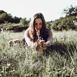 Beautiful young woman practicing yoga on grassy field during sunny day