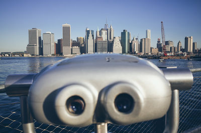 Coin-operated binoculars by river and manhattan against sky