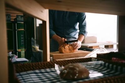 Midsection of man cutting bread in kitchen