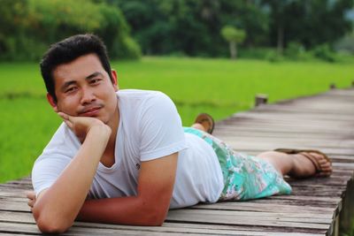 Mid adult man lying on wooden pier over grass field