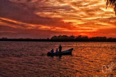 Silhouette people in sea against sky during sunset