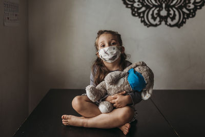 Young girl with mask on sitting and hugging masked stuffed animal negative space