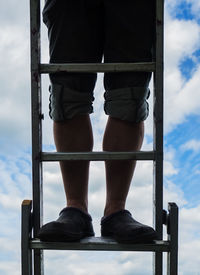 Low section of man standing on ladder against sky