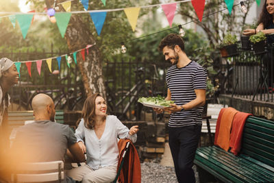 Smiling young woman talking with male friend carrying food during garden party