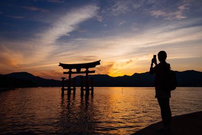 Person taking picture of torii gate at sunset