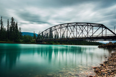 Railway bridge over river against cloudy sky