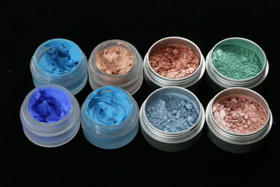 High angle view of colorful make-up product arranged in containers on black background