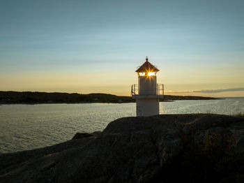 Lighthouse by sea against sky during sunset