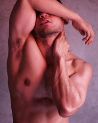Shirtless muscular man covering eyes against wall
