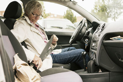 Senior woman fastening seat belt in car