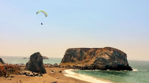 Scenic view of paraglidier and rock formation by beach and sea against sky