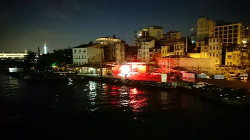 Illuminated cityscape by river against sky at night