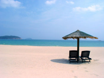 Empty lounge chairs with parasol on sandy beach against sky