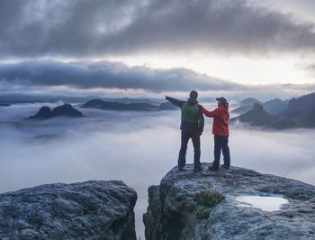 Lovers mirroring in water eye at mountain summit above thick mist. climbing couple at top of summit