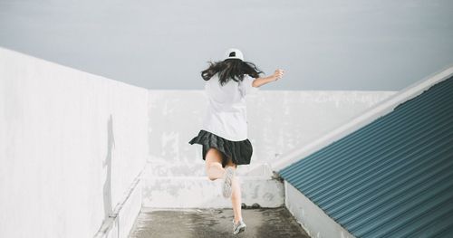 Rear view of woman jumping by wall against sky