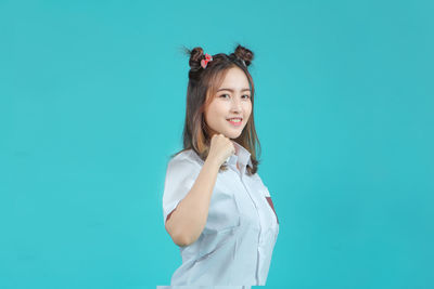Portrait of young woman standing against blue background