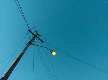 Low angle view of electricity pylon against clear blue sky