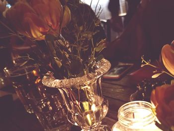 Close-up of lit candle and flower vase by drinks on table in restaurant