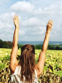 Rear view of woman with arms raised on field against sky