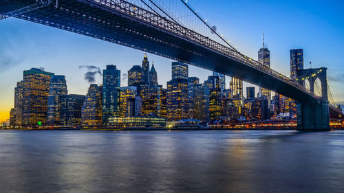 Brooklyn bridge over river against illuminated buildings in city