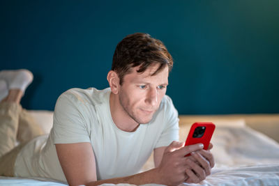 Man resting lying in bed at home looking at smartphone screen, browsing in internet, chatting .