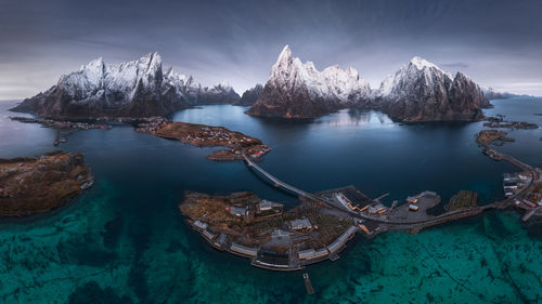 Aerial view of calm water of sea washing island with a village and rocky formations under cloudy sky