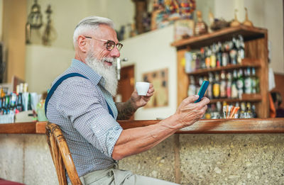 Smiling senior man using mobile phone while drinking coffee at cafe