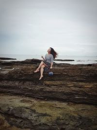 Smiling woman sitting on cliff against cloudy sky