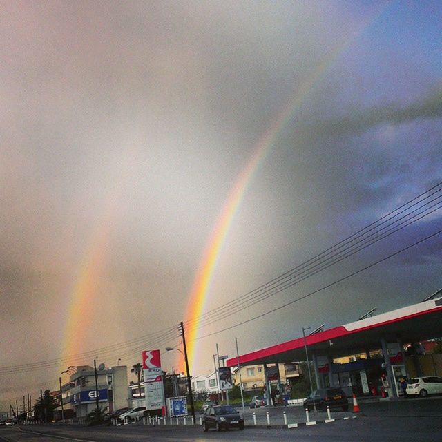 rainbow, sky, transportation, car, multi colored, land vehicle, building exterior, built structure, architecture, road, cloud - sky, mode of transport, street, city, outdoors, weather, cloudy, no people, sunset, low angle view