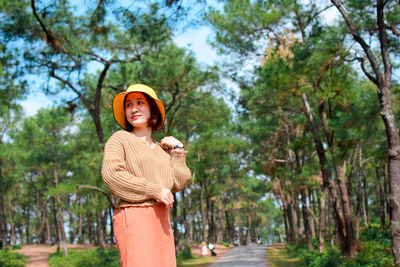 Portrait of smiling young woman standing against trees