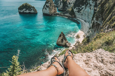 Low section of woman sitting on cliff over sea