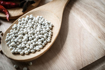 High angle view of white peppercorns with wooden spoon on cutting board