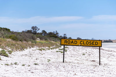 Road closed sign on sandy beach against sky